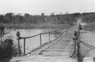 Mawesi-Fluss bei Tunduru : Landschaft mit einer Brücke über einen Fluss. An dem Geländer der Brücke sind Tonköpfe