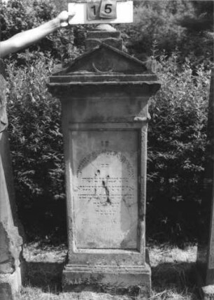 Grabstein 15 (Index: 100113800) Zustand: leicht beschädigt Maße HxBxT: 161x60x28 cm Beschreibung: Stele mit Spitzgiebel und Giebelaufsatz, vertiefter Textteil: Grabstein 15