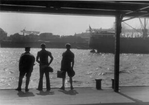 Hamburg. Im Hamburger Hafen stehen drei Seeleute auf einem Schwimmponton der St. Pauli-Landungsbrücken und schauen auf das Wasser. Sie haben sicherlich Sehnsucht nach der Ferne, links die Kuppel des Elbtunnels auf Steinwerder
