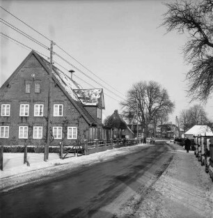 Tremsbüttel-Dorf: Dorfstraße: links Bauernhof Bruno Ruge-Höppner: im Hintergrund weitere Bauernhäuser, davor zwei Pkws: rechts hinten Frau auf Fußgängerweg: Winter