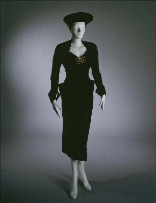 Samtkleid mit Tütentaschen, schwarzer Filzhut mit braunem Netz und schleifenförmiger Brosche (Archivtitel)