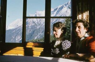 Wanderer an einem Fenster einer Bergbaude mit Blick auf die Berge