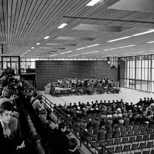 Stormarnhalle: Einweihung: Gäste vorne und rechts unten, dahinter die Bühne mit einem Schulchor