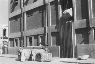 Reisefotos. Arbeiter mit Ballen vor einem Speichergebäude im arabischen Raum (wahrscheinlich in einem Hafen)