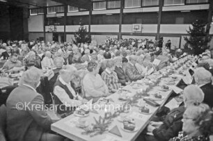 Joachim-Mähl-Schule: Sporthalle: Weihnachtsfeier der Stadt: Senioren an Kaffeetafel: hinten rechts Chor der Matthias-Claudius-Schule und der Joachim-Mähl-Schule: rechts und links geschmückte Weihnachtsbäume: 15. Dezember 1984