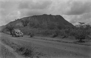 Inselberg (Eruptiv-Schlot, Basalt?) der Feuchtsavanne, vorn: Piste Sanagar-Joko mit PKW