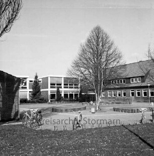Grundschule: Hamburger Straße: ehemalige Volksschule: rechts Altbau: links Erweiterungsbauten: davor Schulhof mit Grünanlage und Baum: vorn Ständer mit Fahrrädern