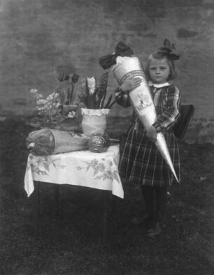 Schulanfängerin mit Zuckertüten, Osterei und Blumen