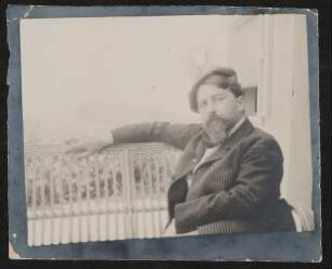 Arthur Schnitzler sitzt im Nadelstreifenanzug mit Mütze auf einer Korbbank