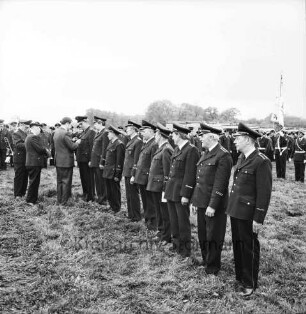 Oetjendorf: Amtfeuerwehrfest: Festwiese: Ehrung für 25-jährige Mitgliedschaft für Gerhard Finnern, Otto Buttgereit, Walter Fobian, Hans Lübke, Wilhelm Rathje, Hugo Taplick, Bernhard Winkelmann, Werner Hinsch und HermannWende durch Kreisbrandmeister Heinz Poschmann und Regierungsrat Alwes: dahinter Feuerwehrmänner: im Hintergrund Häuser und Bäume