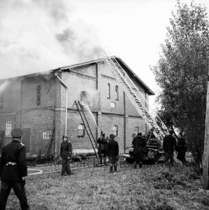 Brand: Wohn- und Wirtschaftsgebäude von Landwirt Adolf Stoffers: brennender Wirtschaftstei mit Rauchschwaden: Giebelfront: davor Feuerwehrleute beim Löschen: rechts Löschfahrzeug mit Drehleiter