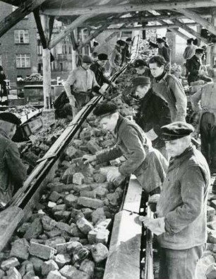 Hamburg-Eimsbüttel. Wiederaufbau. Arbeiter stehen am Förderband einer Trümmeraufbereitungsanlage. Sie sortieren brauchbare Ziegelsteine aus.