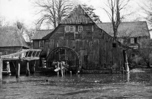 Grander Mühle mit Nebengebäuden: verfallenes Gebäude und beschädigtes Mühlrad: links Brücke: davor Mühlenteich: hinten Bäume