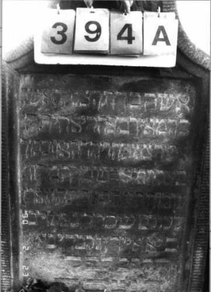 Grabstein 394 (Index: 100115694) Material: Sandstein Zustand: verwittert Maße HxBxT: 112x60x16 cm Beschreibung: Stele mit konkav eingezogenem Segmentbogenabschluß, eingetieftes Schriftfeld Symbolik: Blüte, Ranken: Grabstein 394A