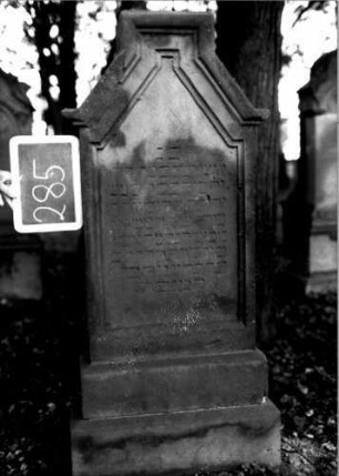 Grabstein 285 (Index: 100111003) Material: Sandstein Zustand: verwittert Maße HxBxT: 134x57x19 cm Beschreibung: Stele, getreppter Sockel, giebelartiger Abschluß, rechteckig erhöht, Schriftfeld eingetieft Symbolik: segnende Hände: Grabstein 285