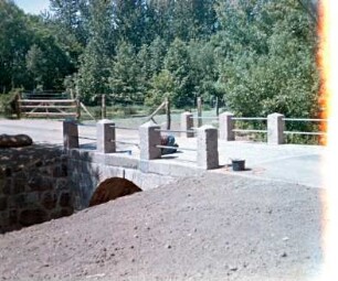Schäperbarg: Granitquaderbrücke über die Barnitz: Sanierung: Fertigstellung: Seitenansicht: Stirnwand, Flügelwand, oben Granitpoller mit Geländer, Arbeiter: im Vordergrund Neuanlage der Böschung