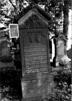 Grabstein 287 (Index: 100112042) Material: Sandstein Zustand: gut Maße HxBxT: 193x72x31 cm Beschreibung: Stele, profilierter Sockel, giebelartiger Abschluß mit Verdachung, rechteckiges Schriftfeld eingetieft, oben mit rund eingezogenen Ecken Symbolik: segnende Hände, geknickte Rose: Grabstein 287