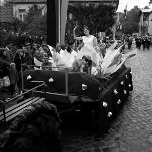 Karpfenfest: Umzug: Matthias-Claudius-Straße / Ahrensböker Straße (hinten): Festwagen, Seerosenkönigin, umgeben von Kindern als Libellen, gezogen von Traktor: links am Straßenrand Zuschauer, Fahnenschmuck, Wimpelgirlande: hinten Musikkapelle, 8. Oktober 1961