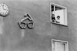 Hausfassade mit Paar am Fenster und Leuchtreklame (Brille)