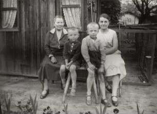 Zwei Frauen und zwei Jungen vor einer Gartenlaube sitzend