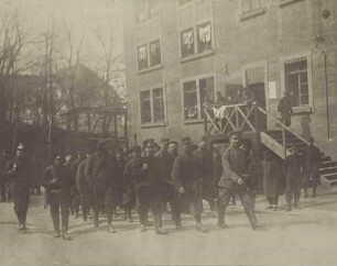 Kriegsgefangene werden unter Bewachung ins Lager geführt, im Hintergrund Fabrikgebäude mit Eingangstreppe