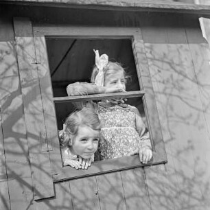 Zwei Mädchen mit Zöpfen und Schleifen schauen aus einem Spielhaus heraus