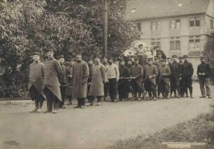 Zweiundzwanzig Kriegsgefangene im Kriegsgefangenenlager Hohenasperg vor einem gezogenen Wagen mit Säcken und Paketen, im Hintergrund Innenhofgebäude