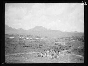 Adwa (Eritrea): Fruchtbare Ebene vor Bergmassiven, im Vordertrund eine Versammlung einheimischer Männer ("Eingeborenentribunal im Freien mit Blick auf Gebirge")