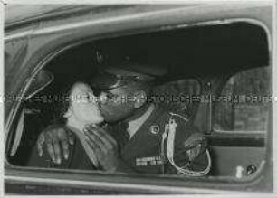 Dunkelhäutiger amerikanischer Besatzungssoldat der Honour Guard küsst hellhäutige Frau auf Autorücksitz