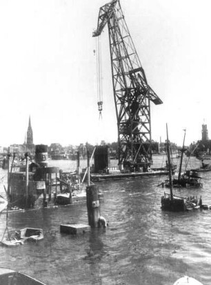 Hamburg. In den Hafenbecken des Hamburger Hafens liegen überall Schiffe auf Grund, die während der Bombardierung der Hansestadt gesunken sind. Sie müssen gehoben werden. Hier ist ein Schwimmkran im Einsatz. Im Hintergrund ist die Silhouette der Hamburger Innenstadt mit dem Nikolaiturm, rechts sogenannter "Kehrwiederturm"/Kaispeicher A