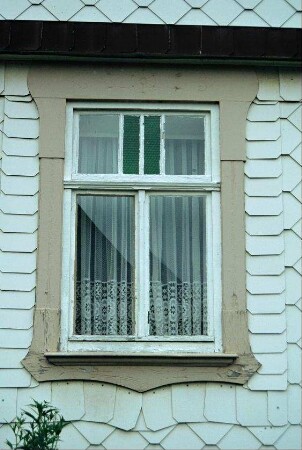 Detail: altes Fenster mit farbigem Glas im Oberlicht, verzierter Blendrahmen