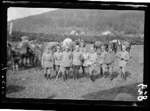 Gruppe von Offizieren vor Pferden auf einer Wiese vor einer bewaldeten Anhöhe