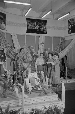 Besucher der Leipziger Herbstmesse 1955 betrachten drapierte Stoffbahnen