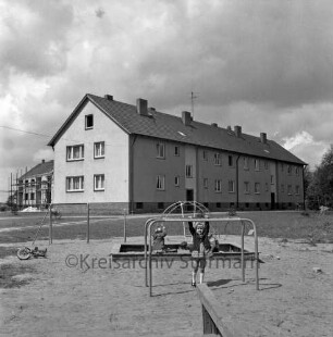 Wohnblock: hinten links Wohnblock im Rohbau mit Gerüst: im Vordergrund Spielplatz mit Kindern im Sandkasten und an Klettergerüst