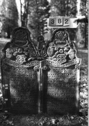 Grabstein 382 (Index: 99752618) Material: Sandstein Zustand: verwittert mit Textverlust Maße HxBxT: 116x98x12 cm Beschreibung: Doppelstele, Schriftfelder eingetieft Symbolik: Pinienzapfen, Trauben, Feigen, Lilien, Ranken, Schriftband, Blüten, Wappenschilder: Grabstein 382