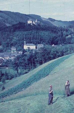 Leutenberg. Blick auf die Stadt mit Stadtkirche (1512) und Friedensburg, im Vordergrund Mann und Frau beim Sensen