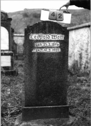 Grabstein 42 (Index: 99798326) Material: Kunststein Zustand: gut Maße HxBxT: 116x51x15 cm Beschreibung: Stele mit zweimal eingezogenem Segmentbogen, Sockel: Grabstein 42