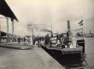 Ägypten. Touristen beim Anlegen in einem Hafen (am Nil oder in Alexandria) mit offenen Lagerhallen für Waren, im Hintergrund Begleitboote der Hapag