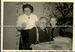 Mutter, Sohn und Großvater am Tisch vor dem Weihnachtsbaum