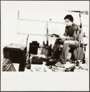 Einzelseite aus dem Booklet der Plattenhülle: Junger Mann sitzt zwischen seinem Musikequipment und Schallplatten