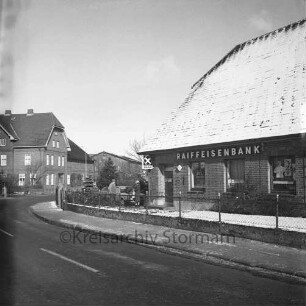 Lasbek-Dorf: Überfall: Raiffeisenbank Bad Oldesloe, Zweigstelle Lasbek: Steindamm: rechts Bankgebäude: links daneben Mann, Frau und Pkw: hinten links Bauernhäuser: Winter