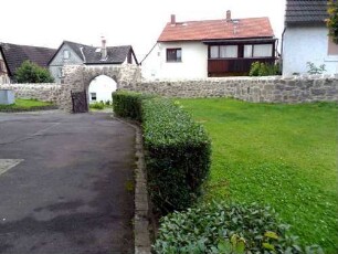 Kirchhof im Westen mit Kirchhofmauer (Wehrgang mit Steinbrüstung und Schießscharten abgetragen) in Übersicht (erhaltener Außenbogen des einstigen Kammertors mit Ansätzen der Zangenmauern)