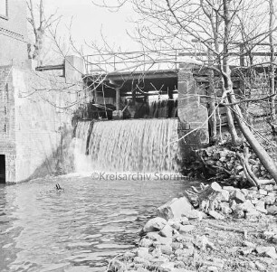Mühlenwehr zwischen Mühlenteich und Glinder Au: darüber baufällige Brücke der Mühlenstraße: rechts Bäume: links Mühlengebäude