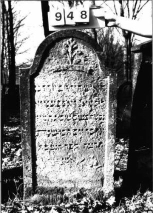 Grabstein 948 (Index: 99753150) Material: Sandstein Zustand: stark verwitt/Textverlust Maße HxBxT: 125x62x10 cm Beschreibung: Stele, eingezogener Rundbogenabschluß, Schriftfeld eingetieft Symbolik: Bäumchen, Band: Grabstein 948