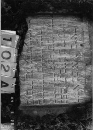 Grabstein 102 (Index: 99792184) Material: Sandstein Zustand: verwittert, unterer Teil der Stele fehlt, Stele liegend Maße HxBxT: 72x64x10 cm Beschreibung: Stele, Spitzbogenabschluß, Schriftfeld eingetieft Symbolik: Zweige: Grabstein 102A