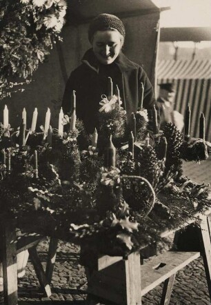 Eine Verkäuferin bietet an einem Stand Adventskränze und Weihnachtsschmuck an