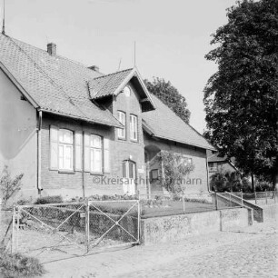 Gemeindebücherei: davor Vorgarten, kleine Mauer und Zaun: hinten rechts Bäume