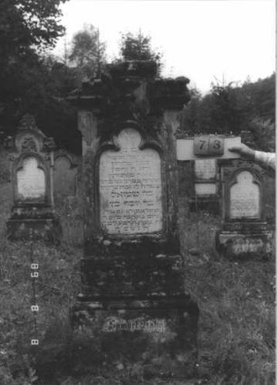Grabstein 73 (Index: 99799553) Material: Sandstein, Schriftplatte Marmor Zustand: verwittert Maße HxBxT: 178x64x27 cm Beschreibung: Stele, Abschluß mit Mittelerhöhung, Sattelverdachung, Zinnenaufsatz, eingelassene Schriftplatte mit Kleeblattbogenabschluß, getreppter Sockel Symbolik: floral: Grabstein 73