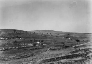 Landschaftsblick : Blick in eine Graslandschaft mit seichten Hügeln und vereinzelten Gebäuden.