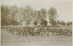 Ulanen in Uniform mit Mütze und Standarten bei Pause auf Exerzierplatz, teils stehend, sitzend oder liegend
